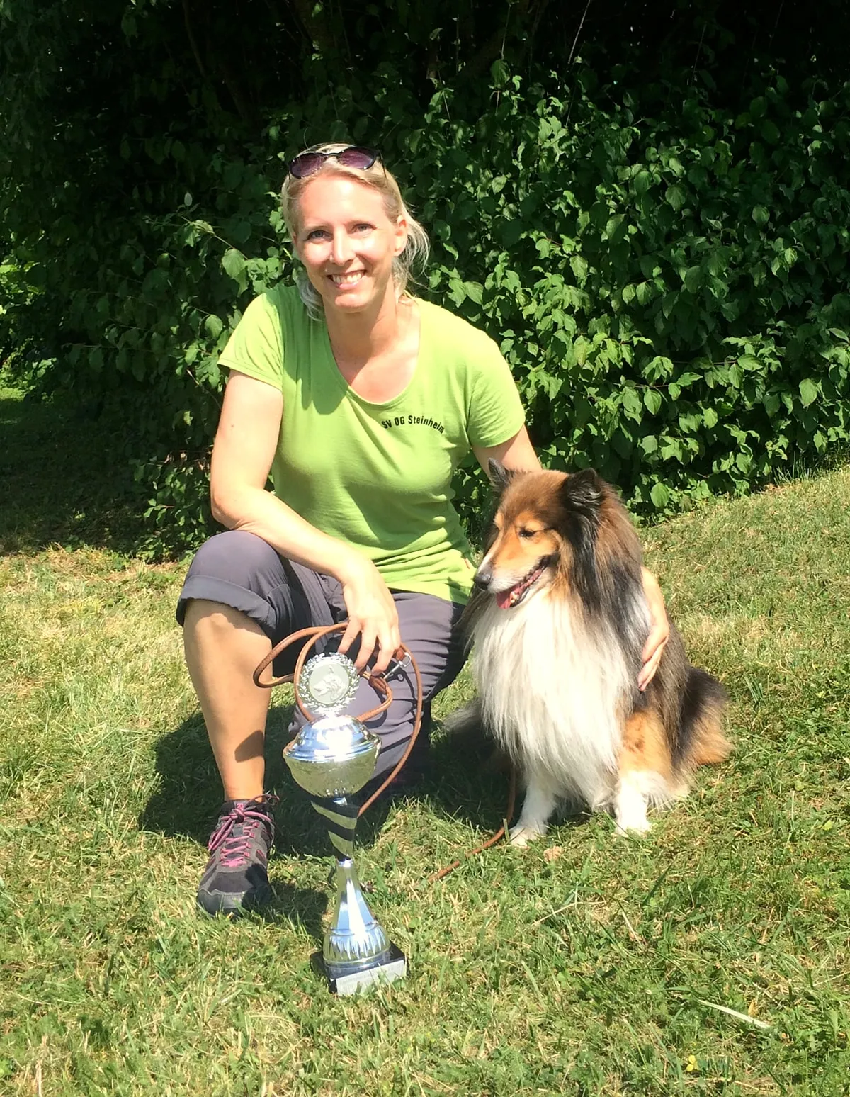 Jana mit ihrem Sheltie und einem Agility-Pokal auf dem Gelände